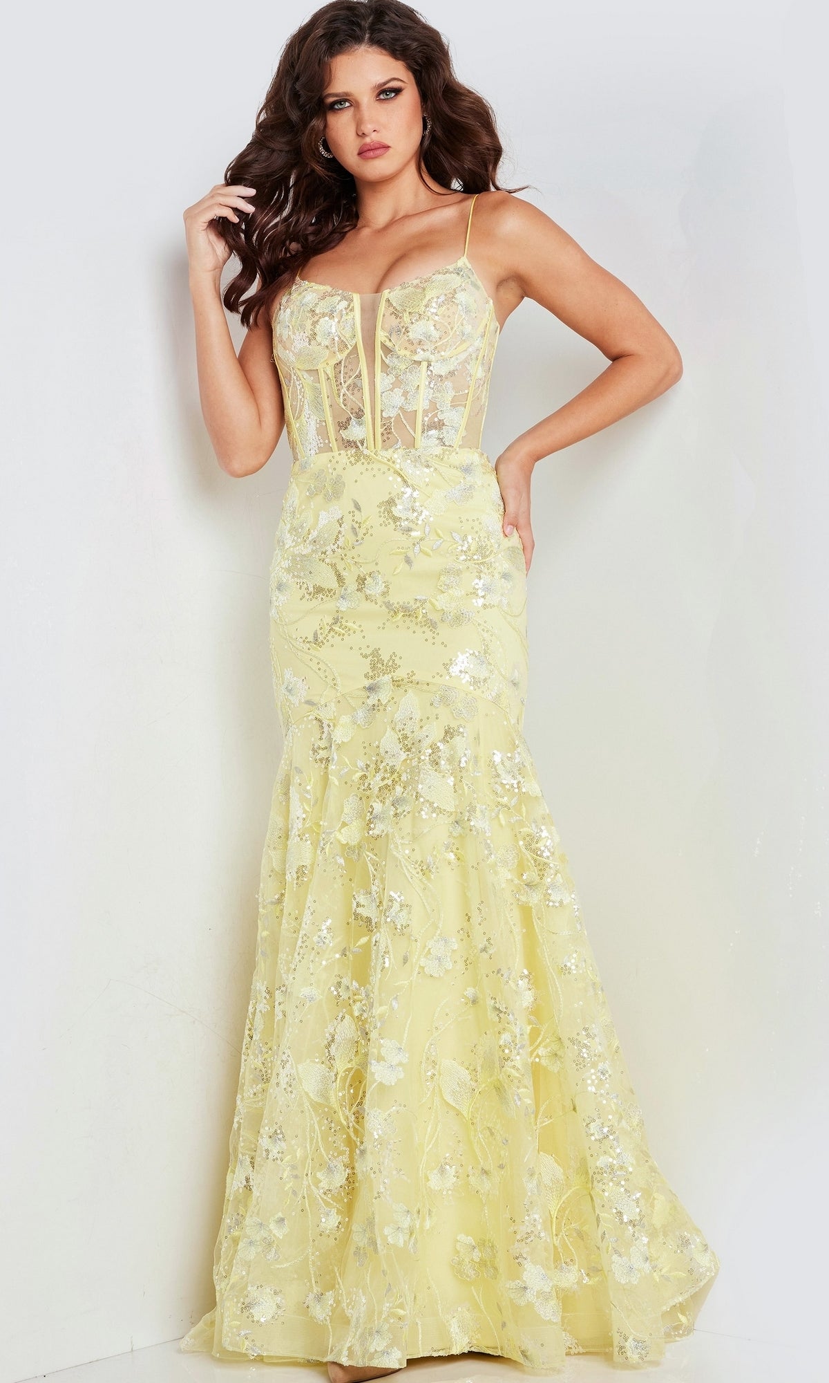 A woman wearing the Long Corset Mermaid Prom Dress: Jovani 38004, a floor-length yellow gown with embroidered lace, thin straps, and a fitted semi-sheer bodice.